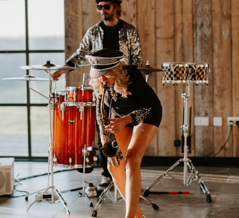 Saxophonist in playsuit, sparkly trainers and hat 