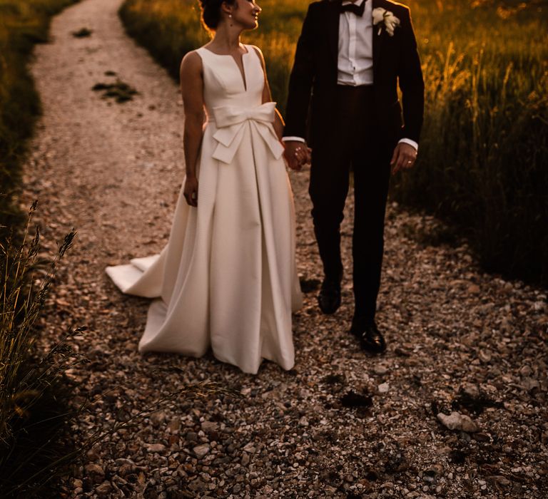 Bride & groom walk together on their wedding day as the sun sets around them