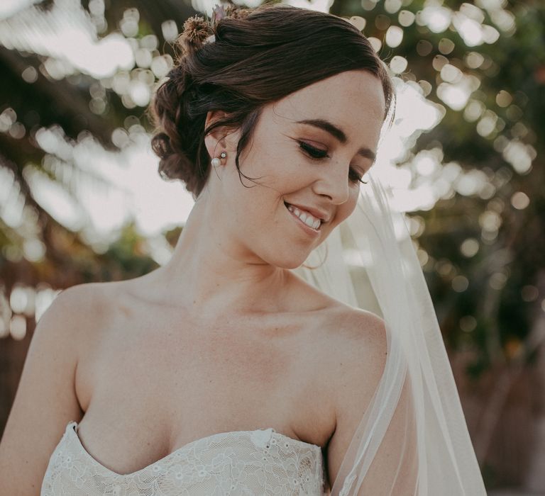 Bride holds her arm across her as she smiles and looks away whilst wearing lace gown on her wedding day