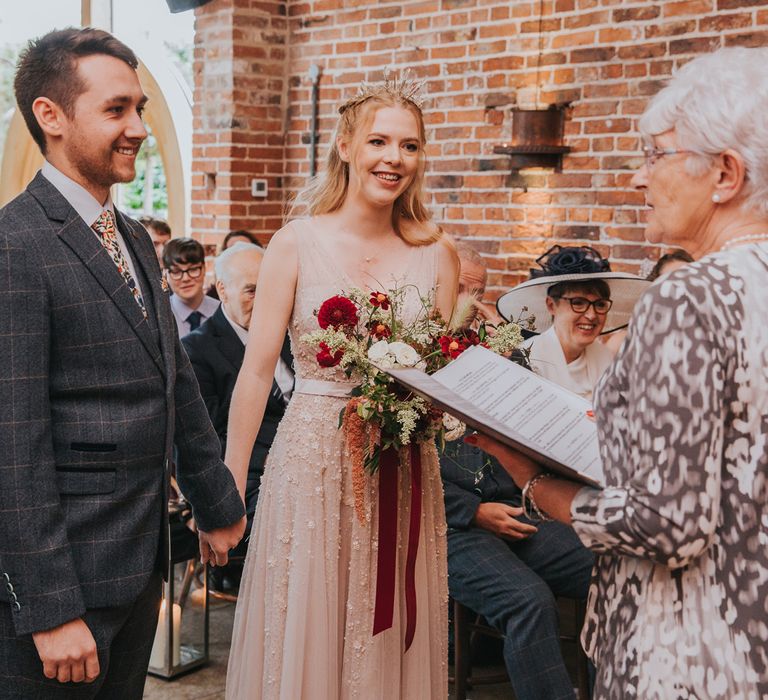 Smiling bride in pearl wedding dress stands with groom in checked suit during barn wedding ceremony