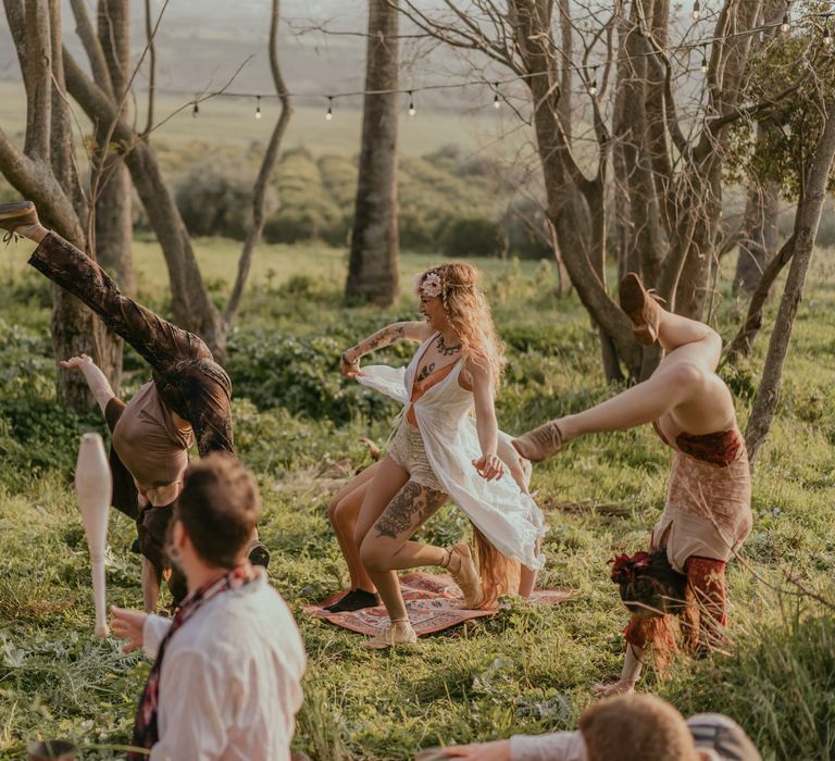 Circus performers and street artists dance within the countryside for hippie wedding reception