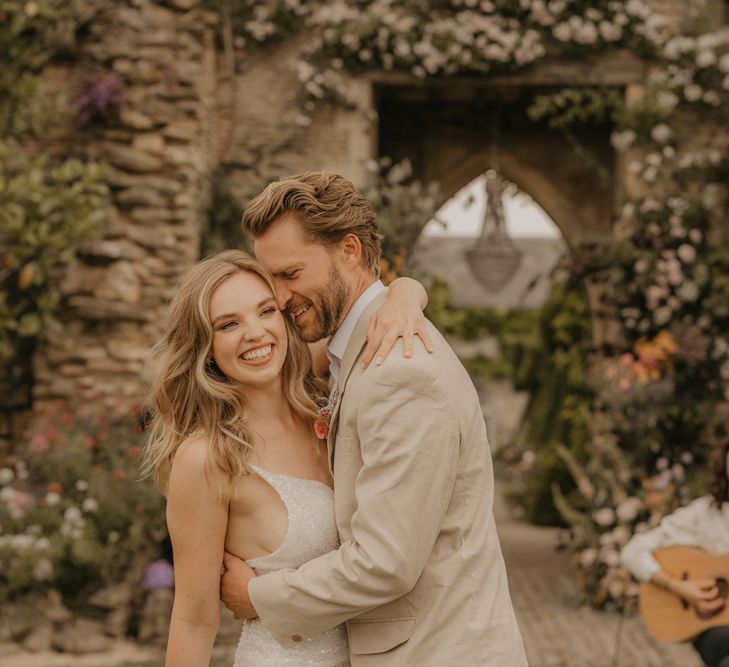 intimate bride and groom portrait as they laugh and dance at their outdoor wedding with the musician playing guitar and singing in the background 