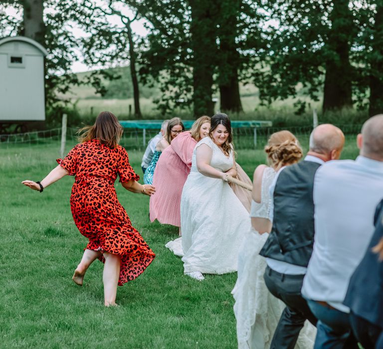 Brides play tug of war outdoors with wedding guests for garden games