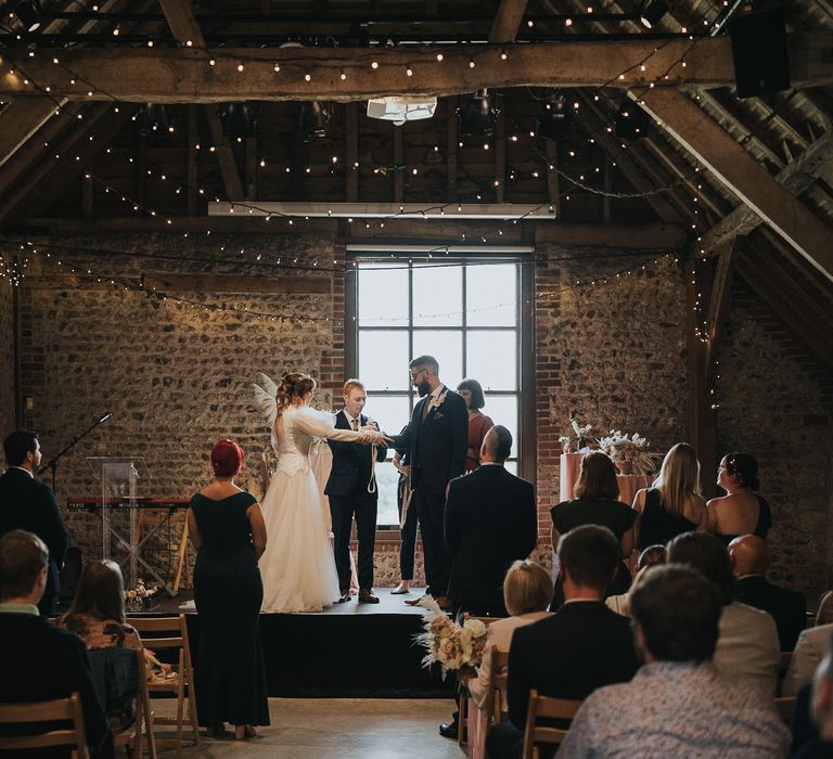 Bride & groom stand at the front of rustic room during their wedding day