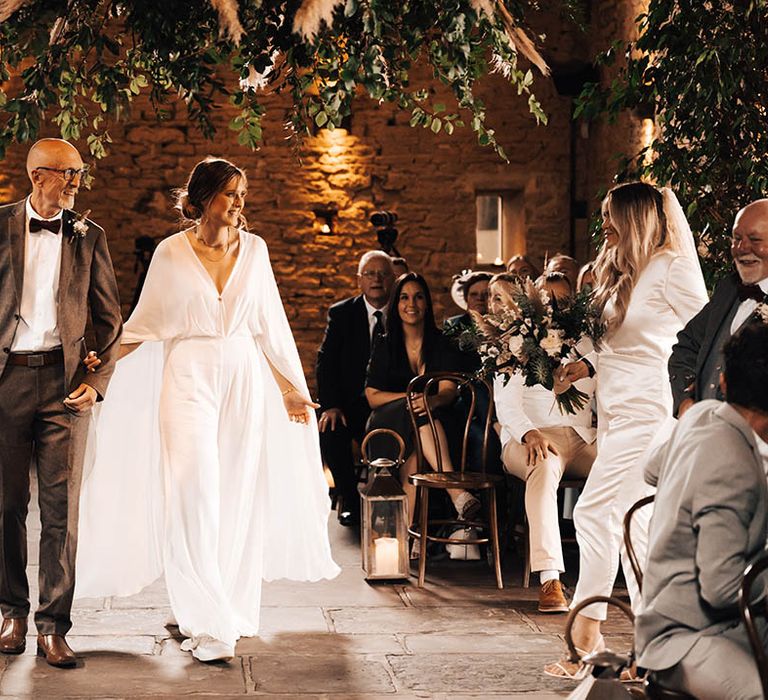 Brides meet one another midway through the aisle with their fathers to continue walking down together