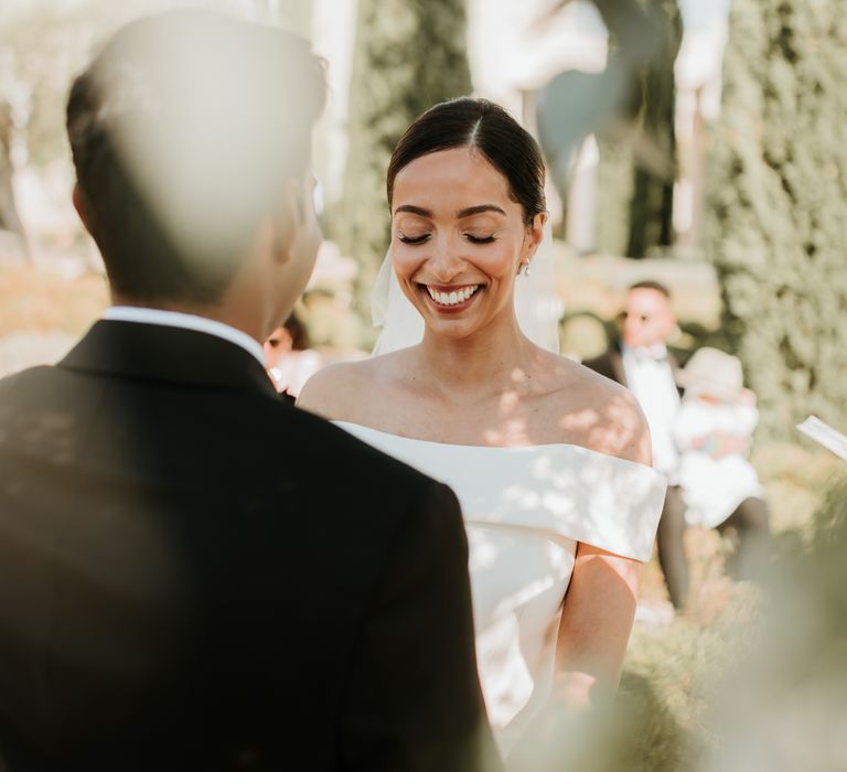 Bride smiles on her wedding day as she wears her dark hair slicked back into sleek low up-do  | Hannah MacGregor Photo & Film