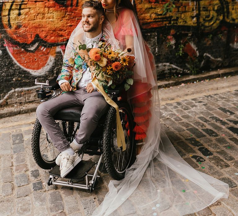 Intimate shoreditch elopement for interabled couple with bride in a coloured wedding dress embracing her disabled groom in a wheelchair 