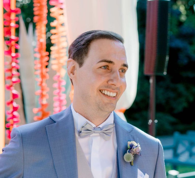 Groom smiles as he wears powder blue suit and silver bow-tie with waistcoat 