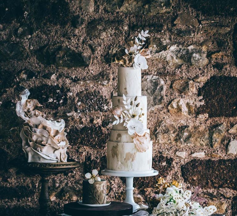 Wedding dessert table with a single tier ruffle cake, and four tier marble cake with floral decor 