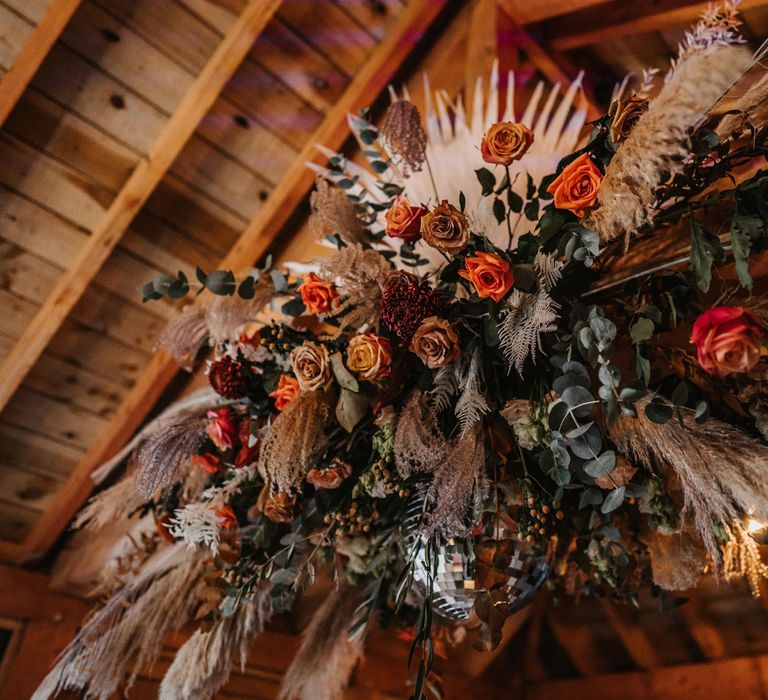 Rustic flower cloud with pampas grass orange and red roses and green foliage for boho wedding at Kinmount House in Scotland