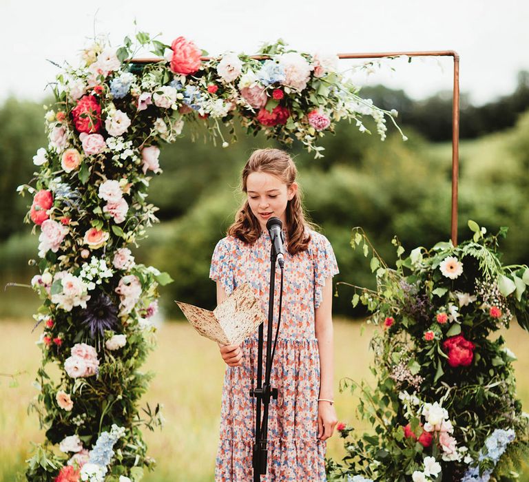 Flower girl gives speech on wedding day under floral arch