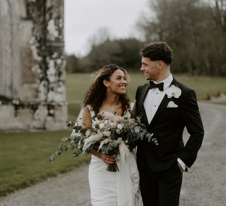 Bride & groom walk together as they look lovingly toward one another as they stand outdoors