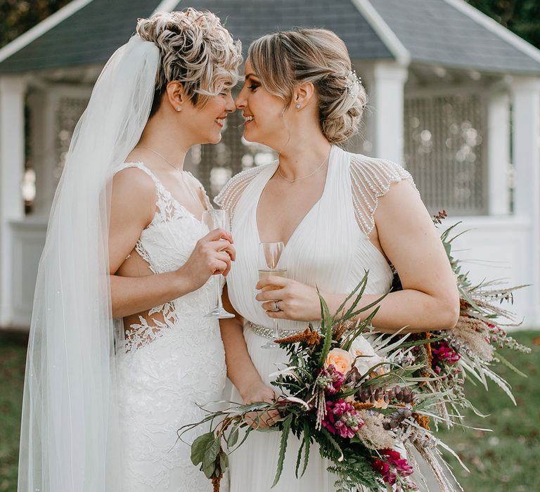 Brides look lovingly at one another outdoors on their wedding day