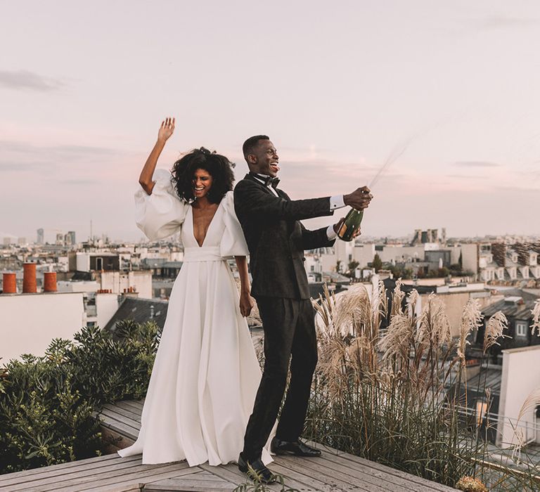 South Asian bride in a princess wedding dress with short puff sleeves and plunging neckline celebrating with her groom in a black tuxedo at their Paris wedding elopement 