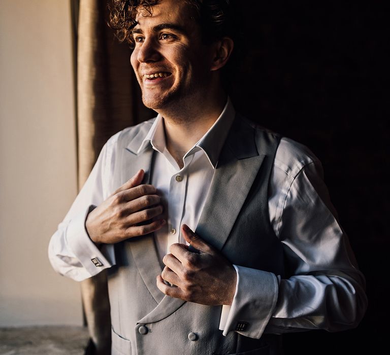 Groom in grey waistcoat gets ready for wedding at Oxnead Hall