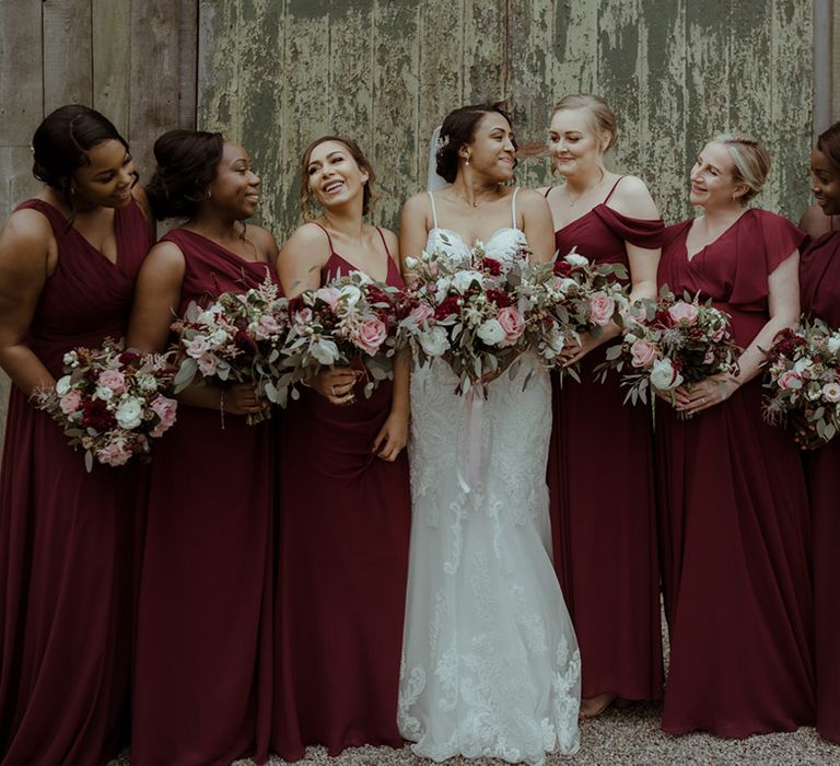 Bride stands with her bridesmaids who wear burgundy bridesmaids dresses 