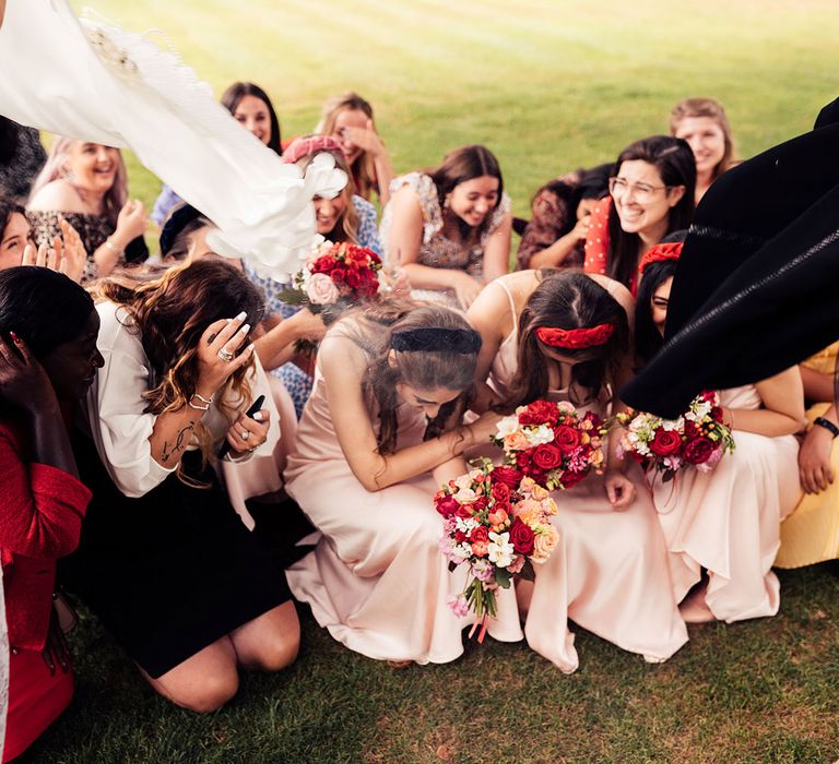 Bridesmaids in pink bridesmaid dresses and wedding guests duck as sugar is thrown on them in traditional sugar ceremony at Iranian inspired wedding