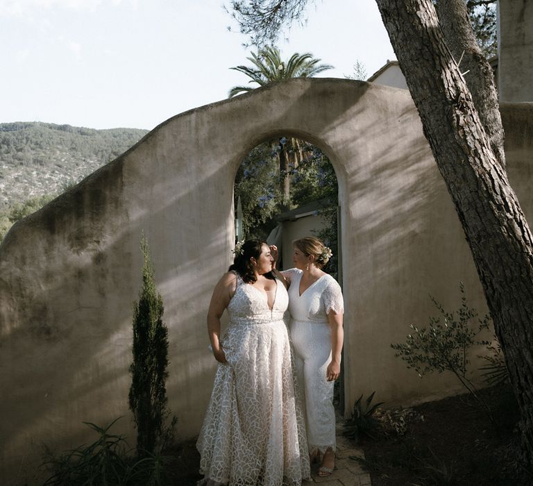 Bride brushes hair out of other bride's eyes as they stand together on sunny day in Barcelona