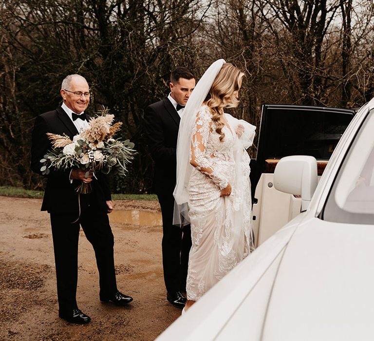 Bride in lace wedding dress gets into white wedding transportation for black tie winter wedding