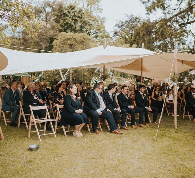 Wedding guests sit outside under cover for outdoor country house wedding