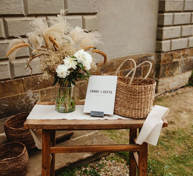 Wooden table and with flowers ingress vase and wicker basket with sign reading 'Cards + Gifts' 