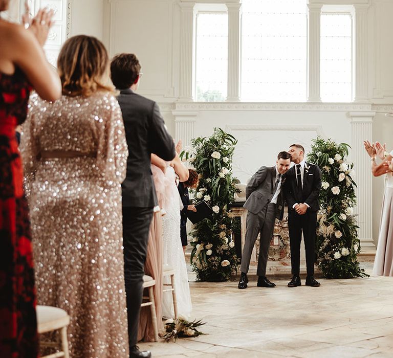 Grooms stand and face their wedding guests after getting married as they clap for them