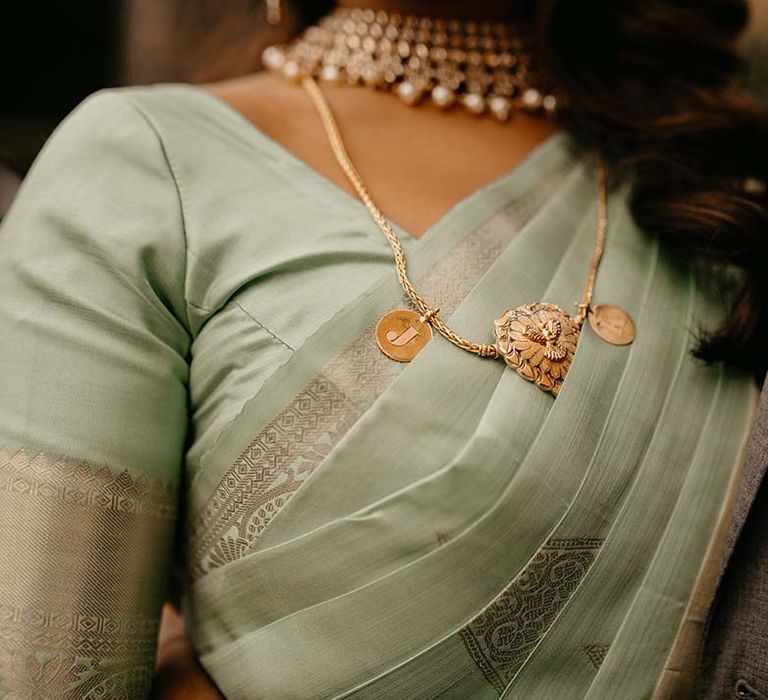 Mint green saree with golden touches, gold and pearl necklace, and a golden J initial necklace pendant 