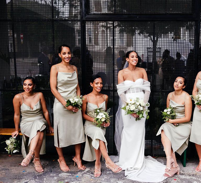 Bridesmaids in sage green cowl neck bridesmaid dresses with bride in off the shoulder corset style wedding dress for industrial wedding