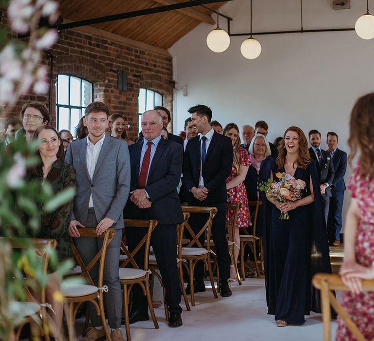 Bridesmaid in navy blue jumpsuit with cape arm sleeves holding colourful bright wedding bouquet for spring wedding