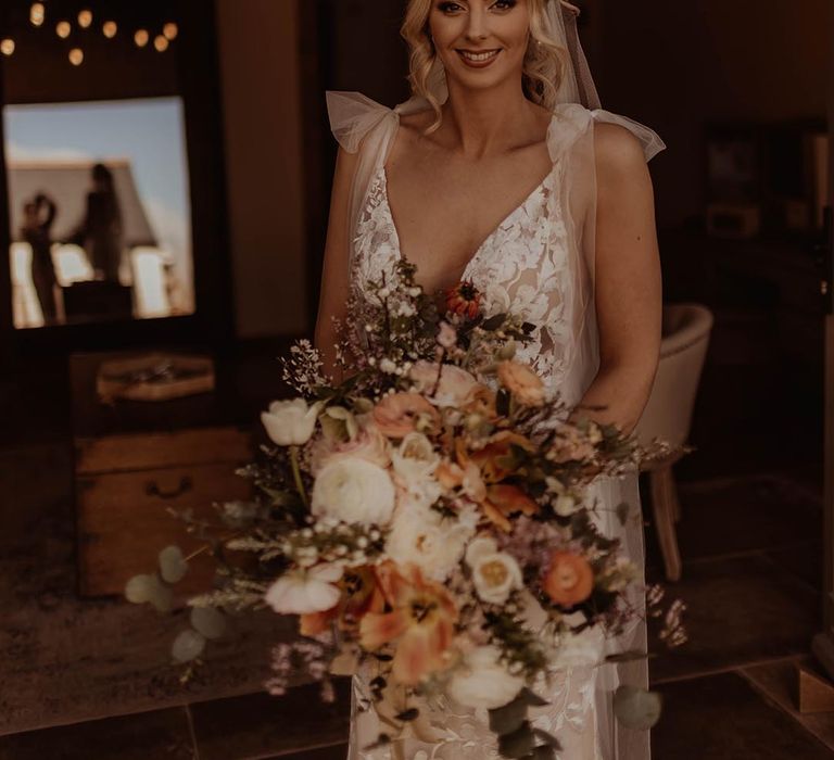 Bride with curled blonde hair wearing a Made With Love wedding dress with bow sleeve detail and autumnal wedding bouquet