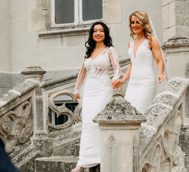 Brides in lace white wedding dresses and matching red lips descend the stairs together 