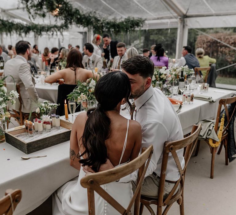 Bride and groom kissing at the top table of their clear glass marquee reception 