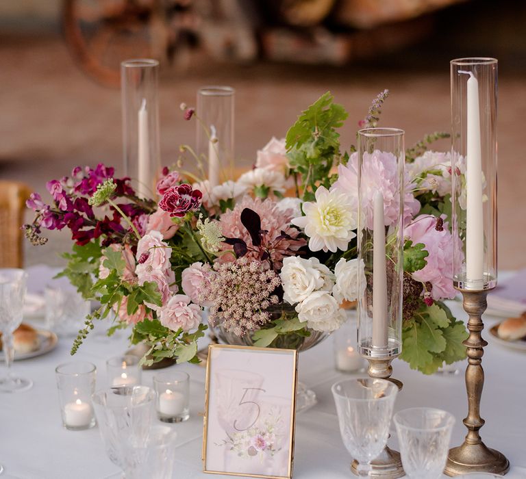 White, purple and pink floral bouquets beside white candles in glass cases 