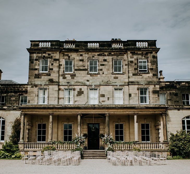 Outdoor wedding ceremony at Birdsall House complete with pastel bouquets lining staircase and white wooden chairs