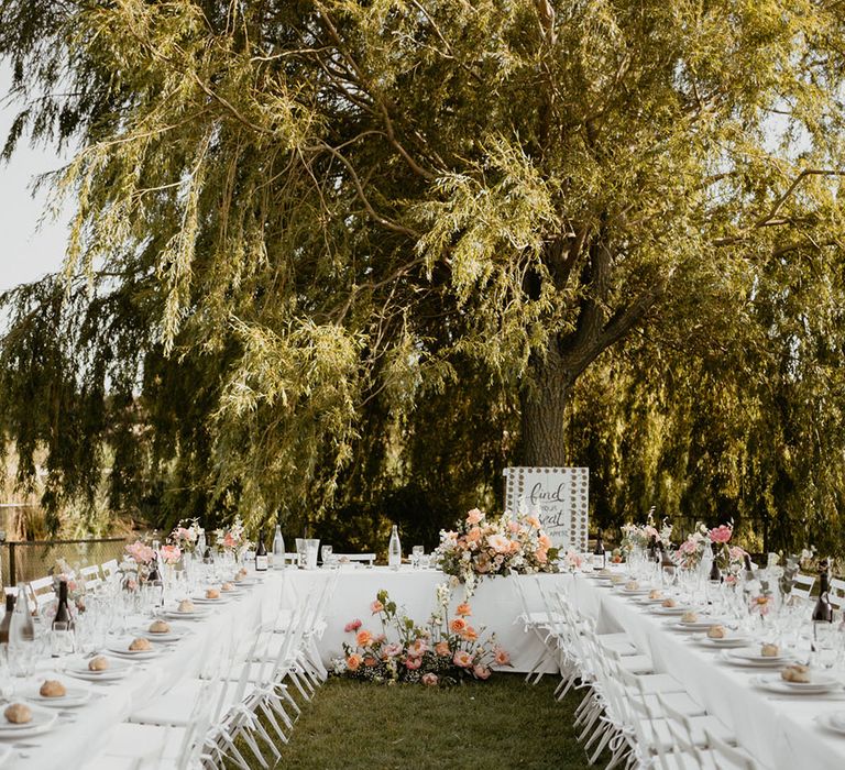 Outdoor wedding reception in France with white tablecloths, large floral arrangements and DIY seating chart pallet to back