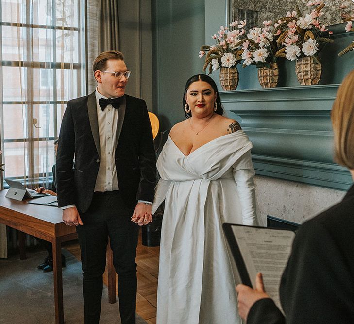 Groom wears black tie and stands with his bride in ASOS curve wedding dress during Old Marylebone Town Hall wedding