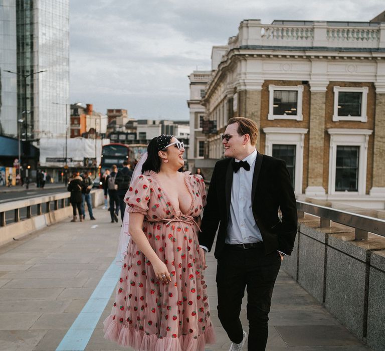 Bride wears white Dr Marten's and pink chiffon dress with glitter strawberries and walks with her groom in black-tie after city wedding ceremony