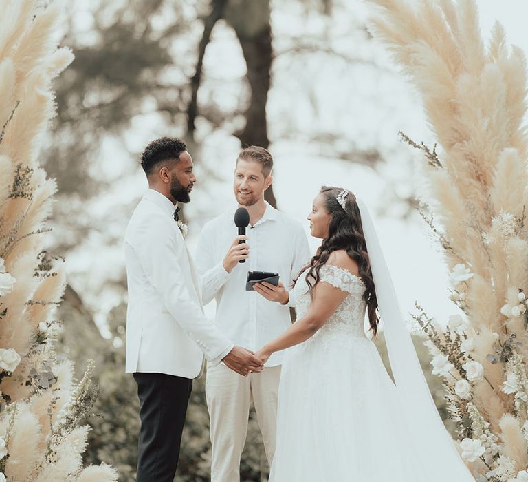 Bride & groom during outdoor wedding ceremony in Phuket surrounded by pampas grass archway 