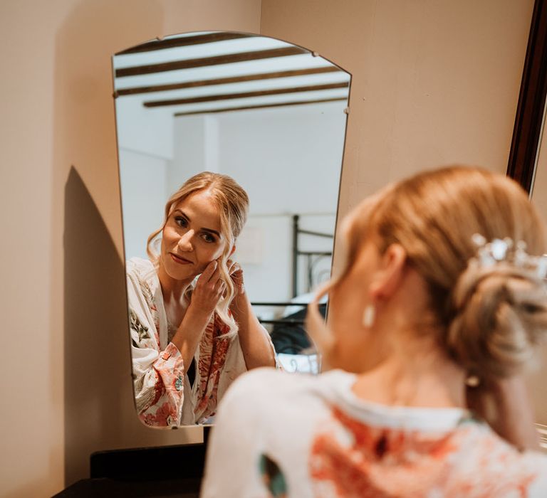 Bride adds earrings on the morning of her wedding day and wears her hair in a chignon complete with curled tendrils to the front 