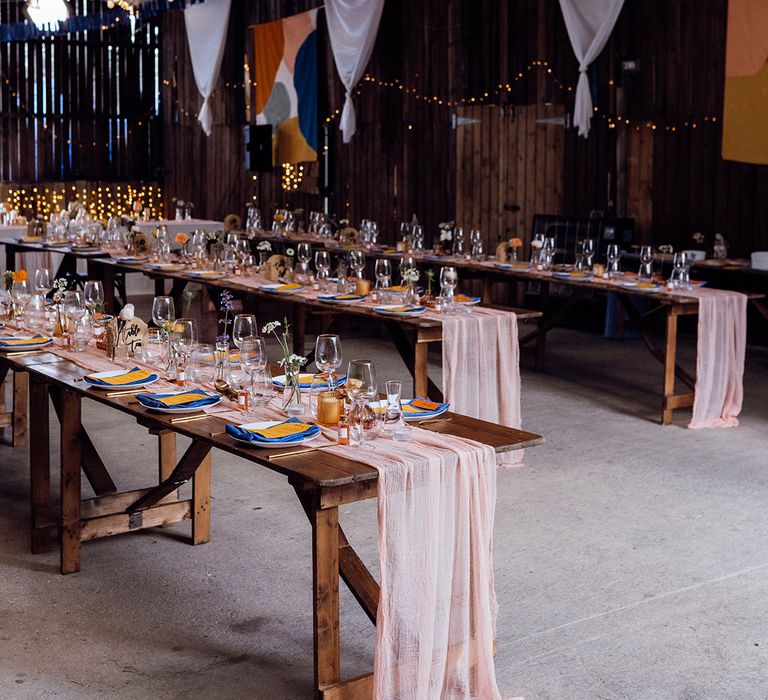 Sheer pink table runners with blue and orange napkins, stationery and candles with fluted glassware and colourful bunting 