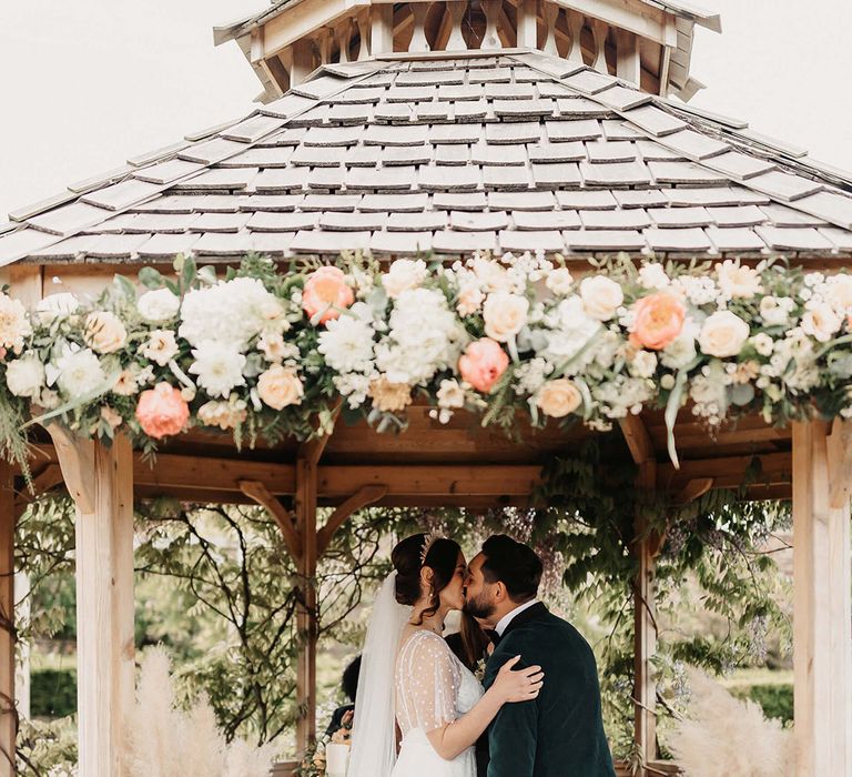 Bride and groom share their first kiss as a married couple with pampas grass decor and flowers around the gazebo