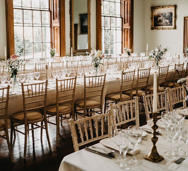 Reception room at Kelmarsh Hall with sage green walls, large framed paintings, minimalistic floral arrangements, minimal table runners and candle holders