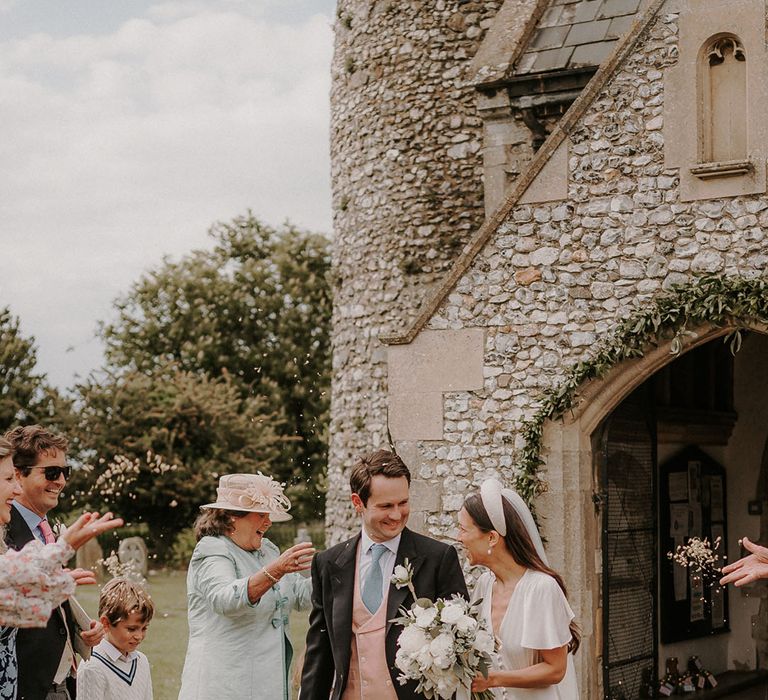 Groom in a morning suit has a confetti moment with the bride in a satin Ghost wedding dress 