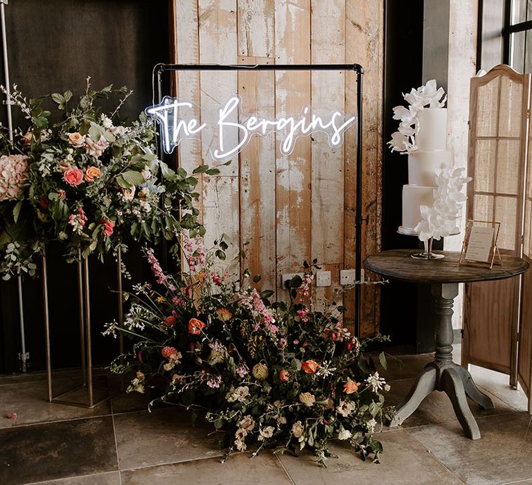 Personalised neon wedding sign beside three tier modern white cake and floral installations 