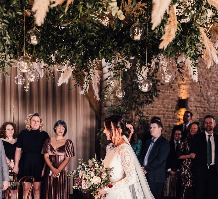 Rustic luxe pampas grass cloud with winter decor with the bride in a long sleeve wedding dress walking down the aisle 