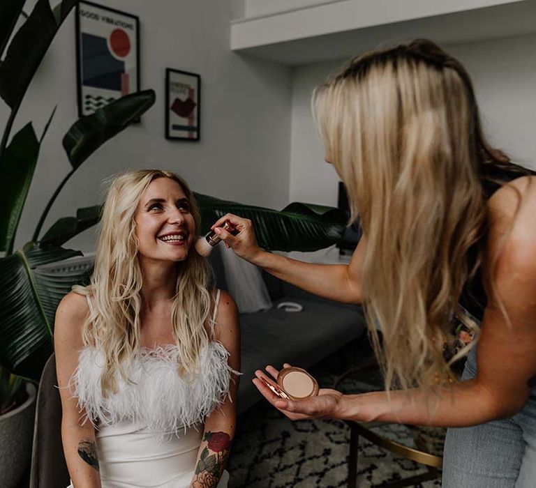 Bride in feathery, fluffy detailed top getting her makeup done before stylish wedding at Hackney Studios