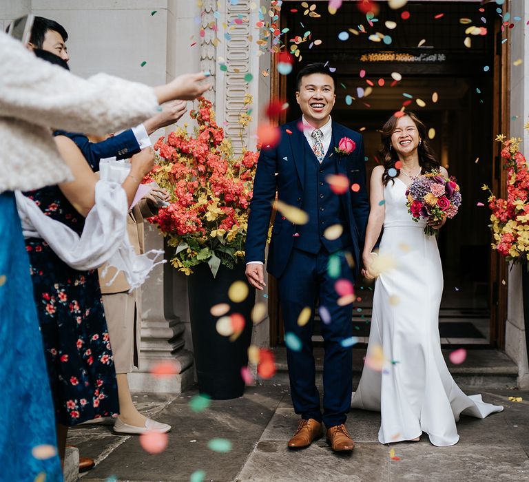 Bride & groom walk out of the Old Marylebone Town Hall as colourful confetti is thrown around them