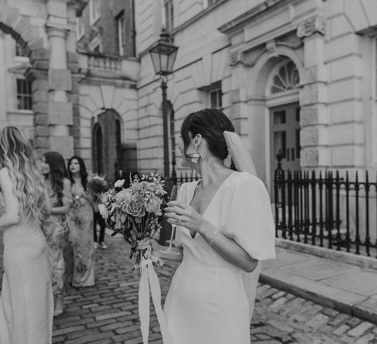 Bride in v neck puff sleeve wedding dress holding neutral toned floral bouquet and a glass of champagne 