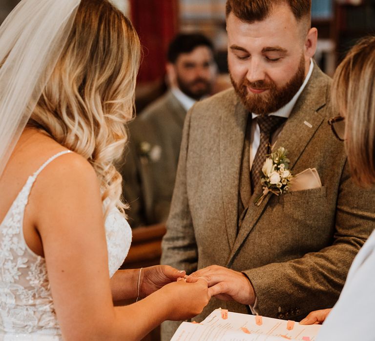 Groom in a grey suit and bride in a lace wedding dress put on their wedding ring for the church ceremony 