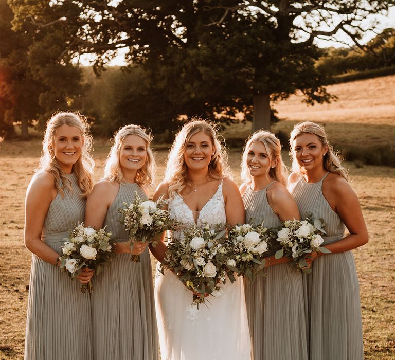 Smiling bridal party with the bridesmaids in a sage green pleated bridesmaid dress and the bride in a Christina K lace wedding dress 